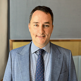 A man wearing a grey suit smiles at the camera.